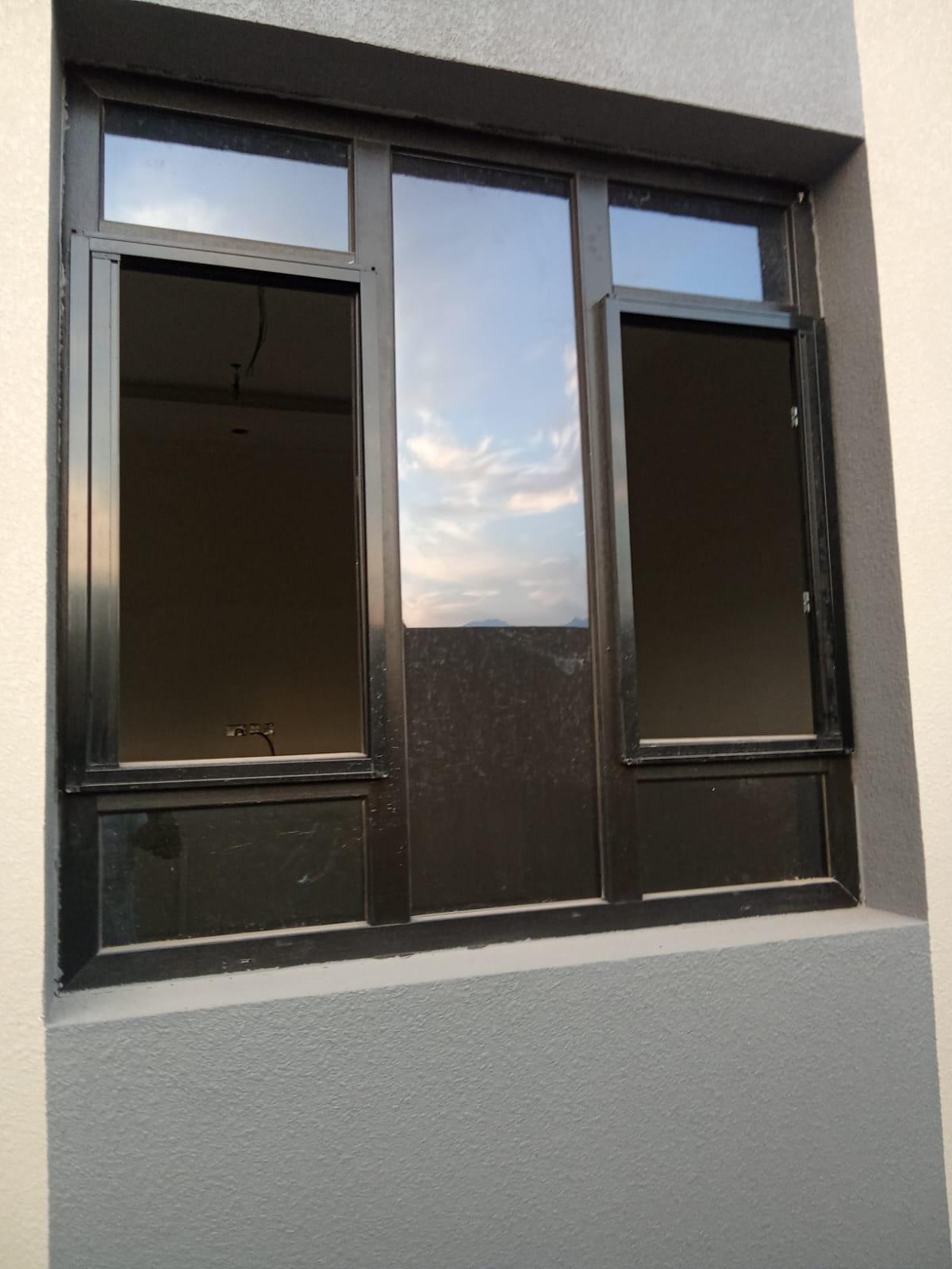 Nine-pane black aluminium window reflecting Oman sky